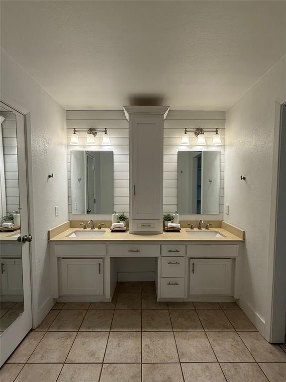 8513 Ravenswood Road Granbury, TX 76049 - Photo 16 of 21 Dual vanity with sinks, light-toned countertops, white shaker-style cabinetry, continued shiplap and a central built-in storage tower. The closet is to the left and separate shower and toilet are the the right.