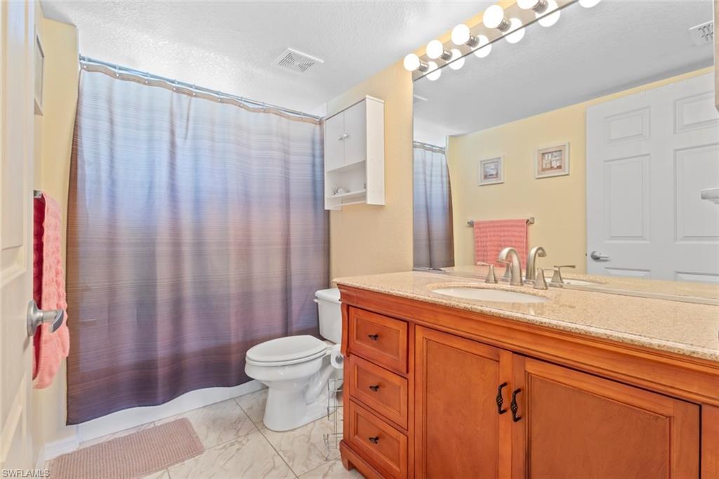 8288 Key Royal Lane, Unit 1435 Naples, FL 34119 - Photo 16 of 26 a bathroom with a granite countertop sink a toilet a mirror and shower curtain