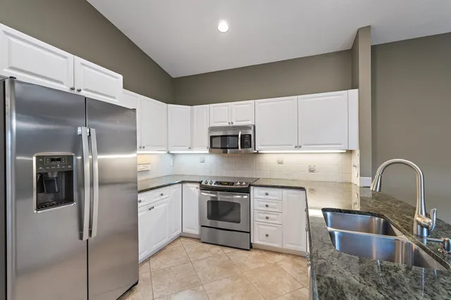 a kitchen with stainless steel appliances granite countertop a refrigerator a stove a sink and white cabinets