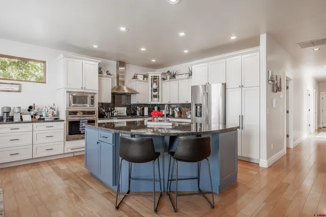 a kitchen with stainless steel appliances kitchen island granite countertop a refrigerator a stove a sink dishwasher and a dining table with wooden floor