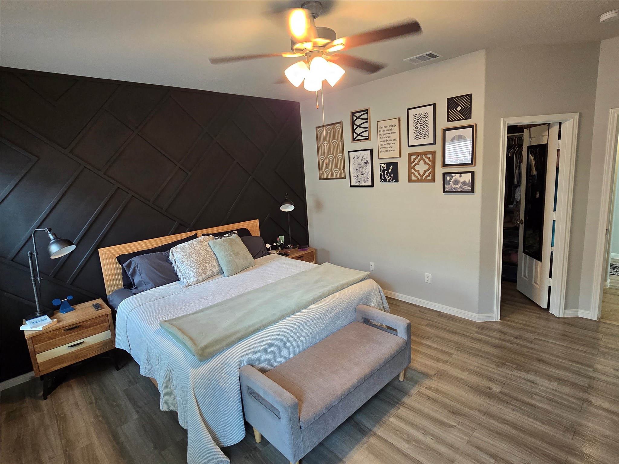 1942 Bending Green Drive Rosharon, TX 77583 - Photo 17 of 30 This spacious bedroom features a stylish dark accent wall, cozy bed with modern side tables, and a ceiling fan. The room is decorated with framed art and has easy access to a walk-in closet, creating a comfortable and inviting space.