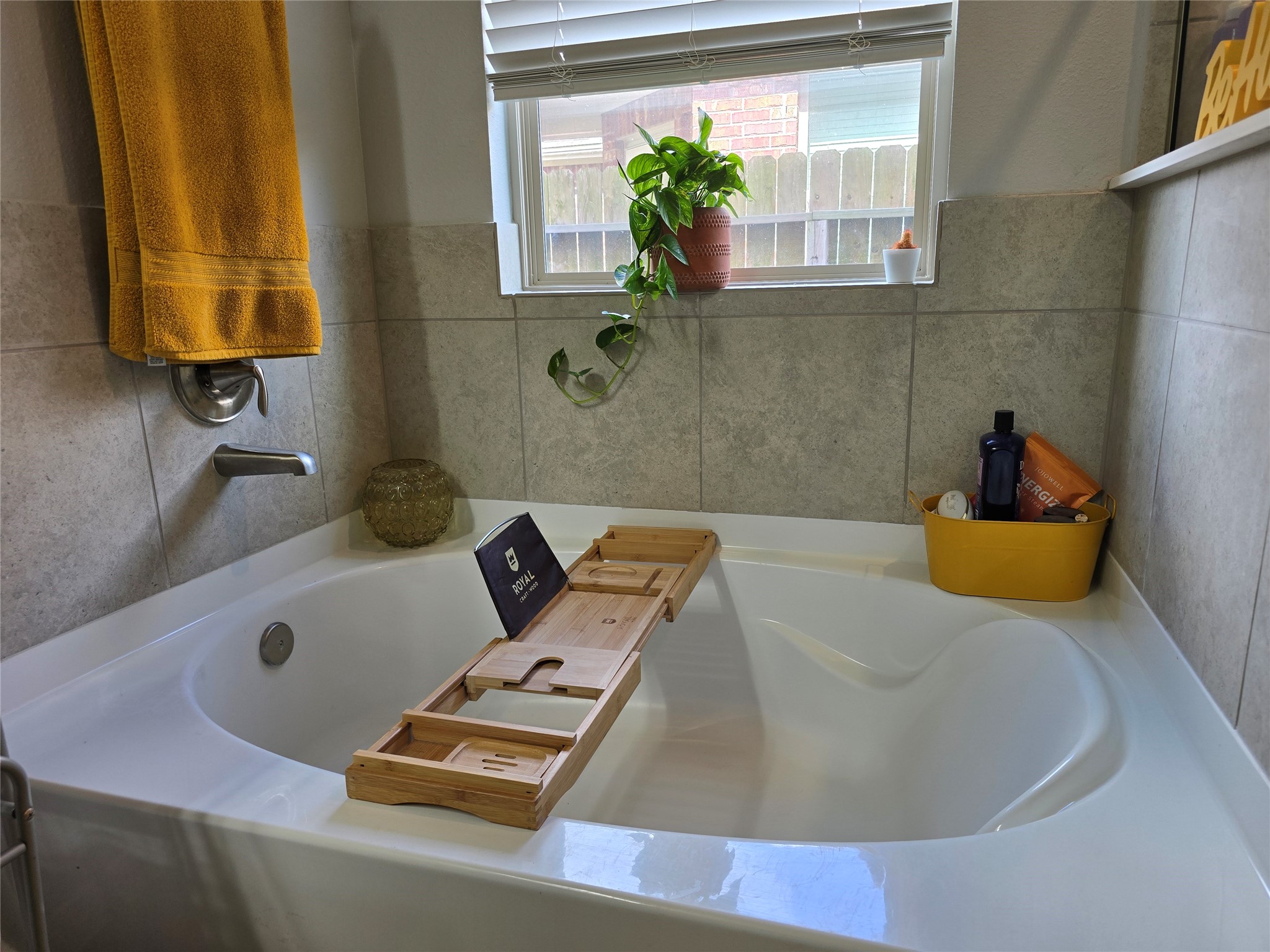 1942 Bending Green Drive Rosharon, TX 77583 - Photo 19 of 30 This bathroom features a cozy bathtub with a tile surround, a handy caddy for relaxation essentials, and a window providing natural light. A potted plant and neatly arranged toiletries add a touch of comfort and style.