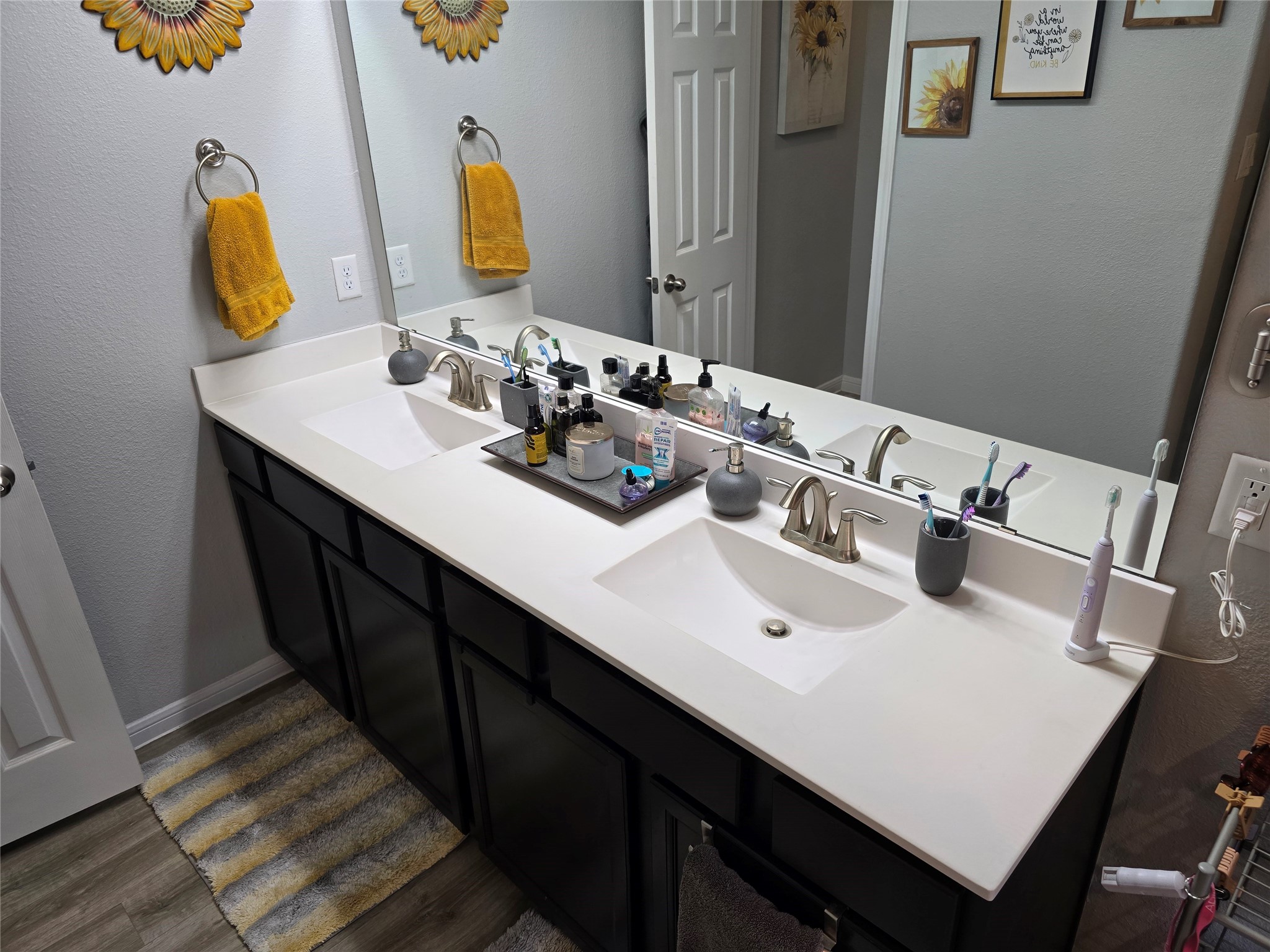1942 Bending Green Drive Rosharon, TX 77583 - Photo 21 of 30 This bathroom features a modern double vanity with sleek white countertops and under-mounted sinks. The large mirror enhances the sense of space, complemented by elegant fixtures and dark cabinetry. Bright yellow accents add a cheerful touch.