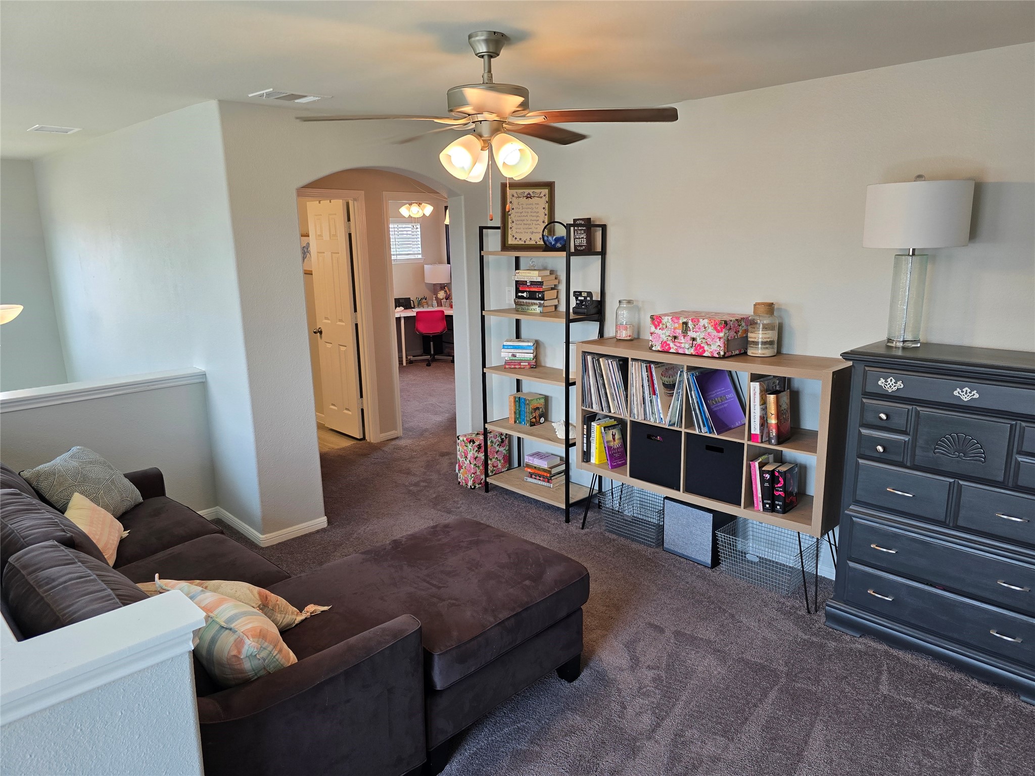 1942 Bending Green Drive Rosharon, TX 77583 - Photo 22 of 30 This cozy living area features a comfortable sectional sofa, ceiling fan, and ample natural light. A hallway leads to additional rooms, while a stylish shelving unit and dresser offer storage. The space is carpeted, creating a warm atmosphere.