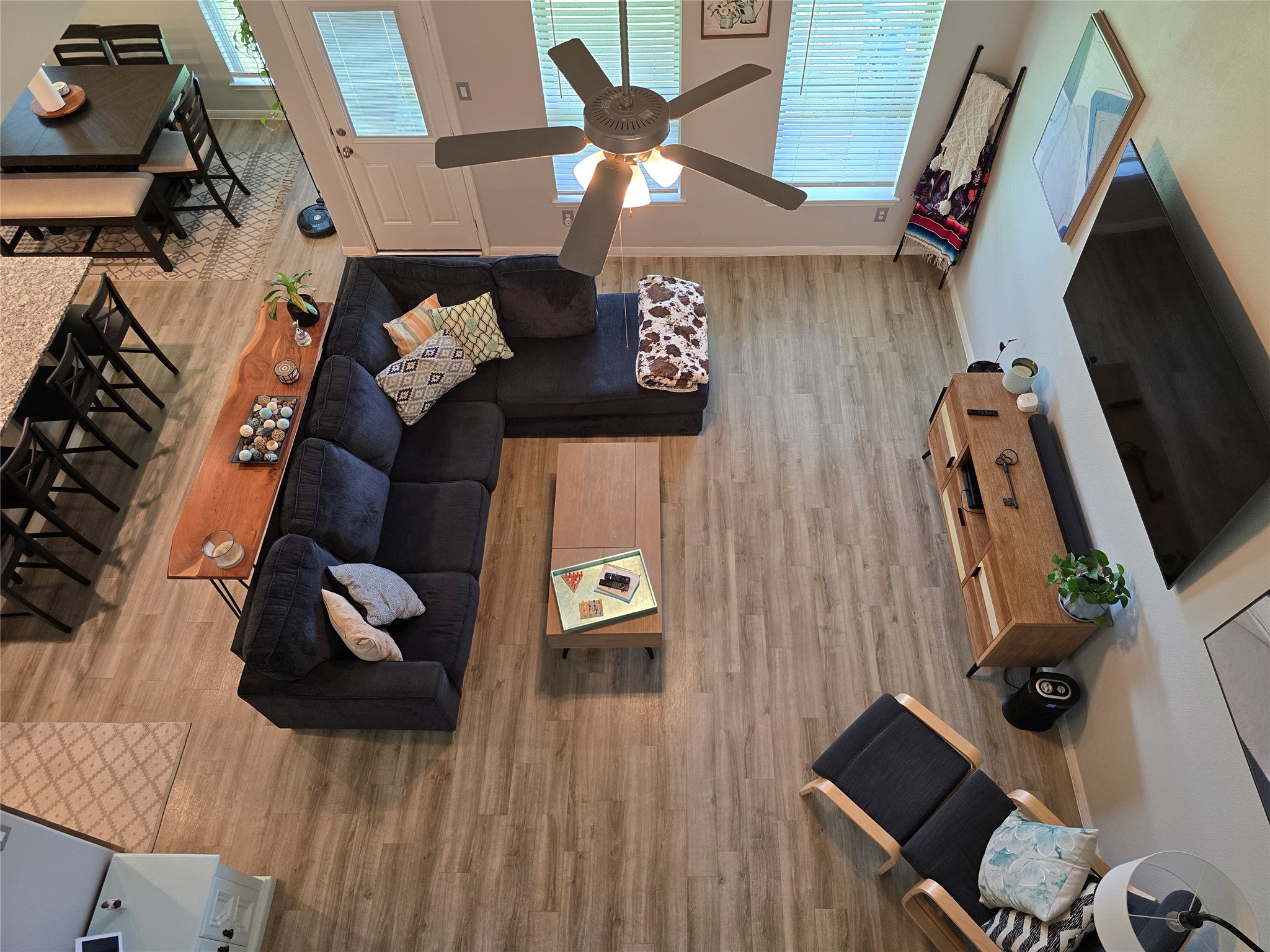 1942 Bending Green Drive Rosharon, TX 77583 - Photo 23 of 30 This spacious living room features a modern, open-concept design with a comfortable sectional sofa, stylish wood flooring, and ample natural light from large windows. A ceiling fan and a cozy seating area enhance the inviting atmosphere, while a dining area and kitchen are visible, providing a seamless flow for entertaining.