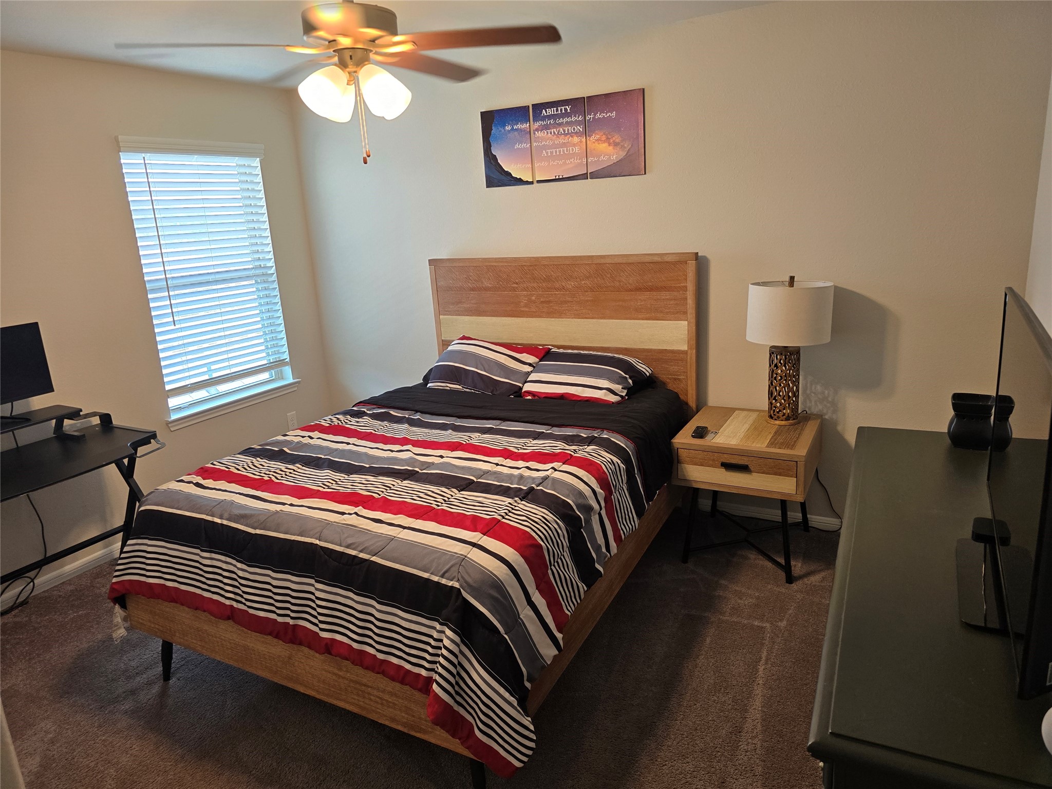 1942 Bending Green Drive Rosharon, TX 77583 - Photo 24 of 30 Cozy bedroom featuring a double bed with a striped comforter, a bedside table with a lamp, and a ceiling fan. The room has a window with blinds, neutral walls, and carpeted flooring, creating a warm, inviting atmosphere.