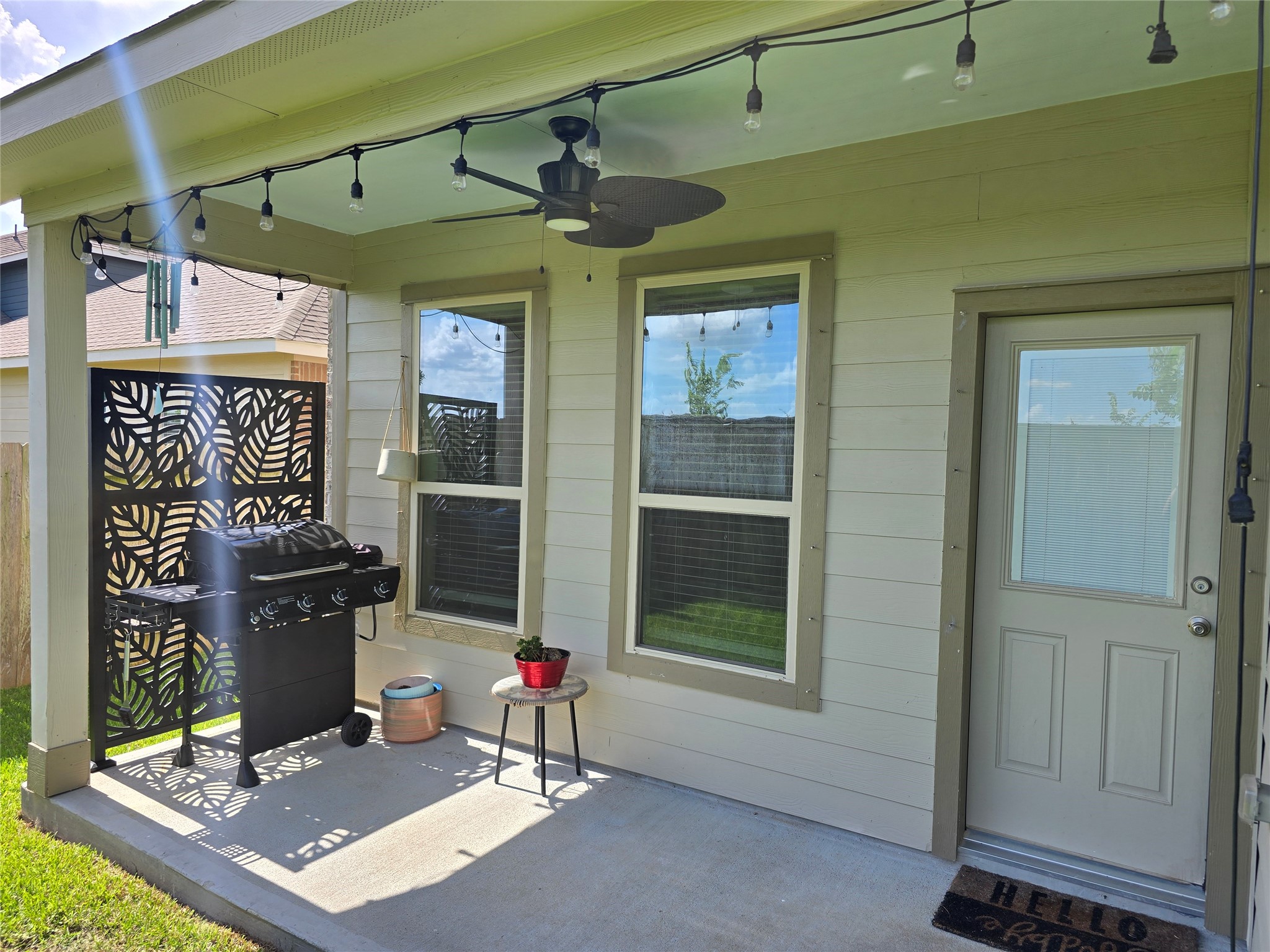 1942 Bending Green Drive Rosharon, TX 77583 - Photo 29 of 30 This cozy patio features a covered area with string lights, a ceiling fan, and a grill. It's ideal for outdoor entertaining with a decorative privacy screen and a small table for added convenience.