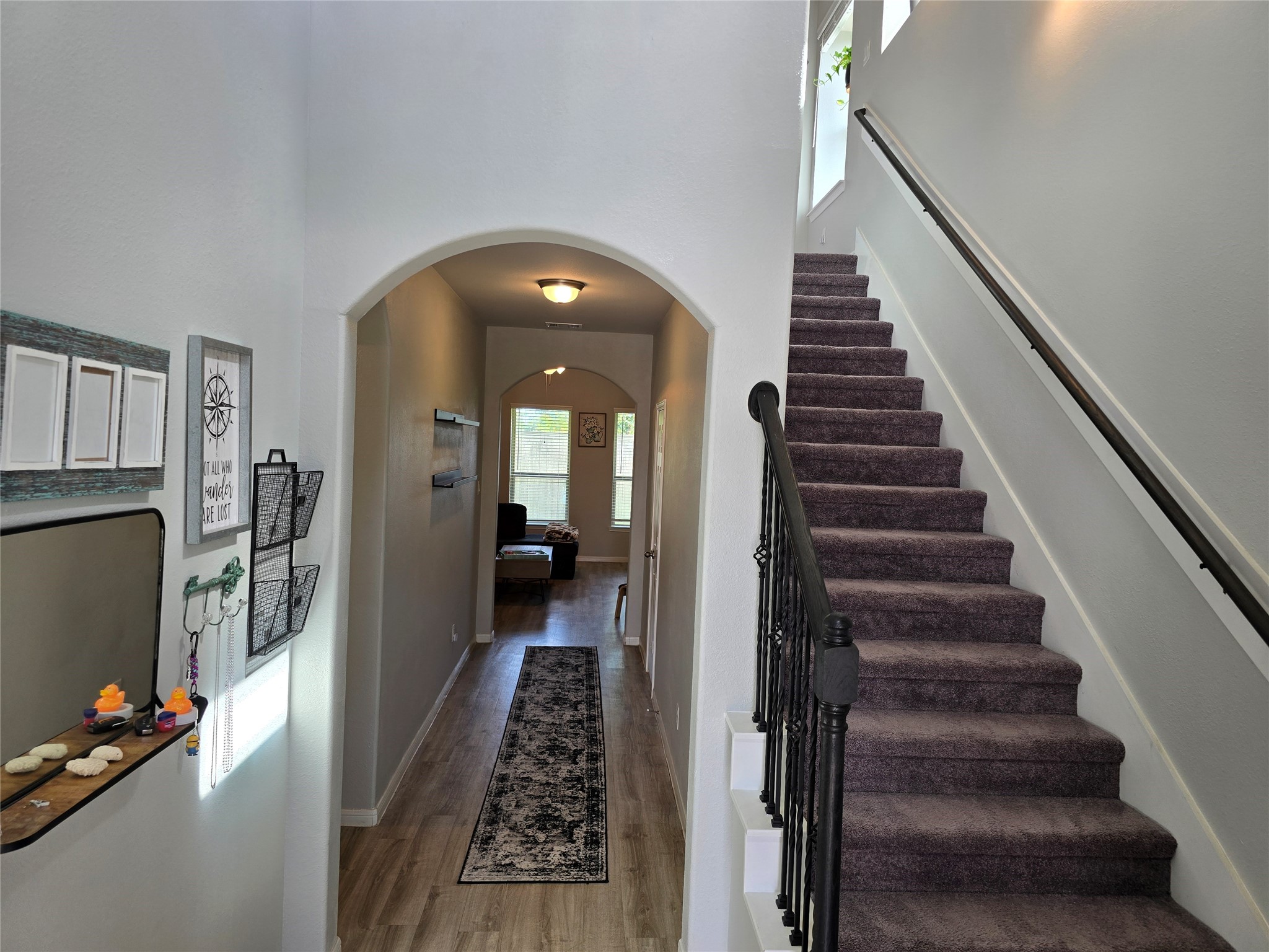 1942 Bending Green Drive Rosharon, TX 77583 - Photo 3 of 30 This photo shows a welcoming entryway with a carpeted staircase on the right and a long hallway leading to a bright living space. The area features neutral walls, wooden flooring, and decorative elements for a cozy feel.