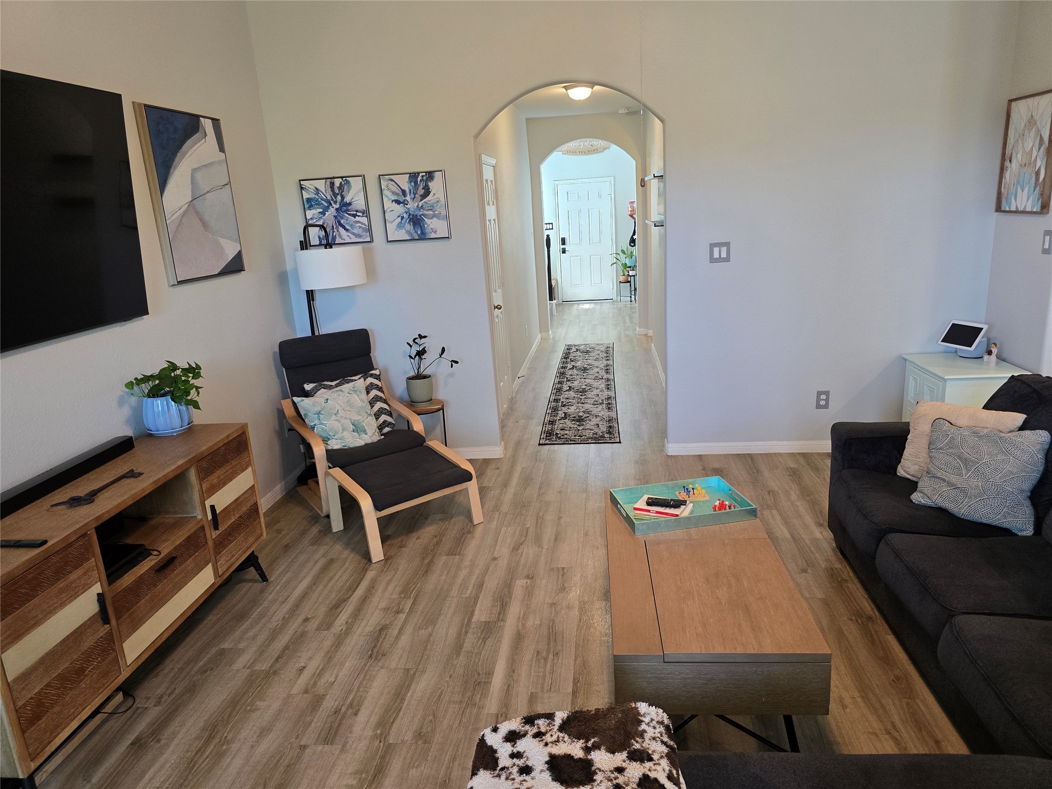 1942 Bending Green Drive Rosharon, TX 77583 - Photo 7 of 30 This inviting living room features modern decor with a sleek flat-screen TV, comfortable seating, and stylish artwork. The space is bright with light wood flooring and a glimpse into a welcoming hallway leading to the rest of the home.