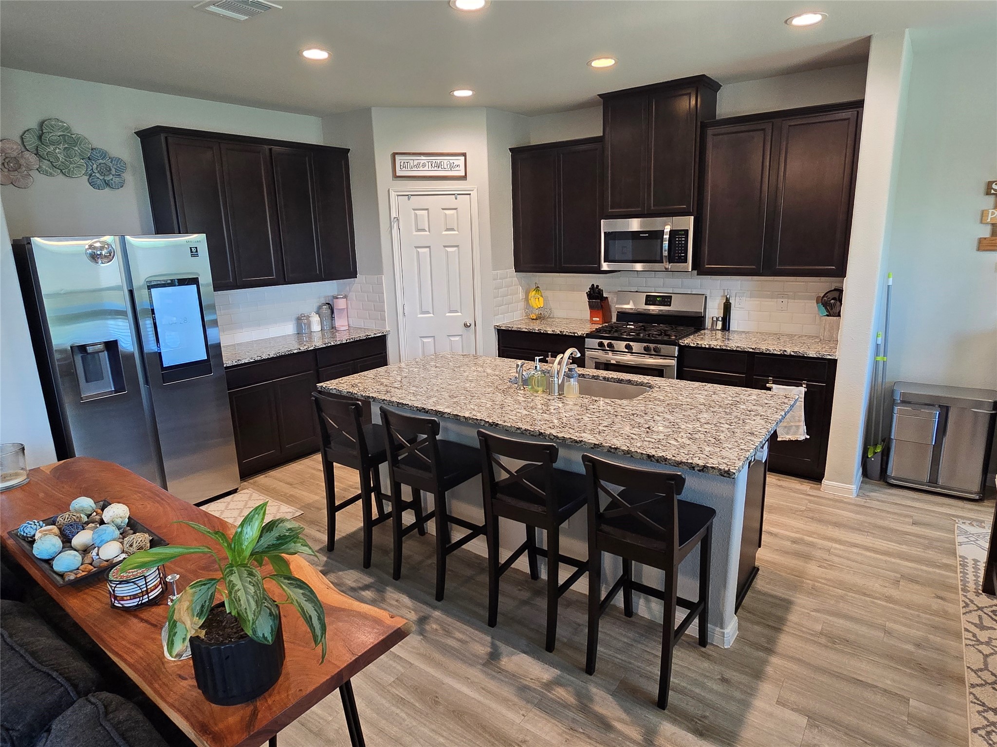 1942 Bending Green Drive Rosharon, TX 77583 - Photo 8 of 30 This kitchen features modern stainless steel appliances, dark cabinetry, and a large central island with a granite countertop and seating. It's complemented by light wood flooring and recessed lighting, offering a stylish and functional space for cooking and gathering.