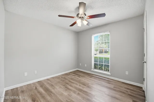 an empty room with wooden floor chandelier fan and windows