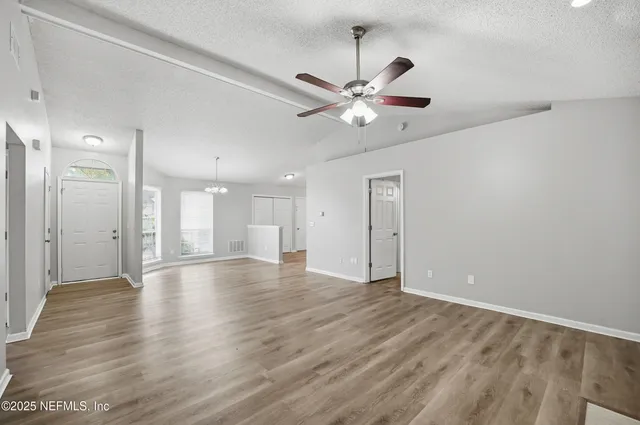 a view of an empty room with wooden floor and a ceiling fan