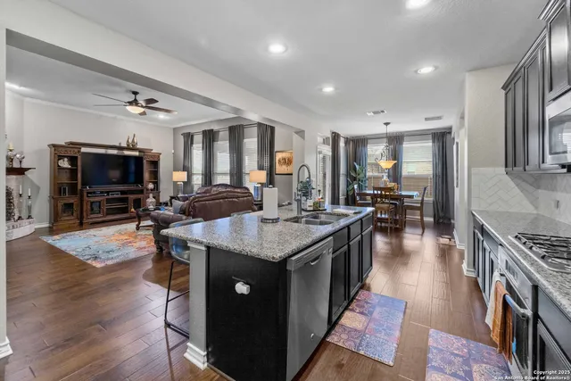 a kitchen with granite countertop a stove top oven a sink dishwasher a dining table and chairs with wooden floor