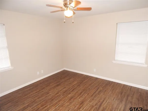 an empty room with wooden floor fan and windows