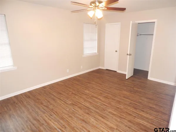 an empty room with wooden floor fan and windows