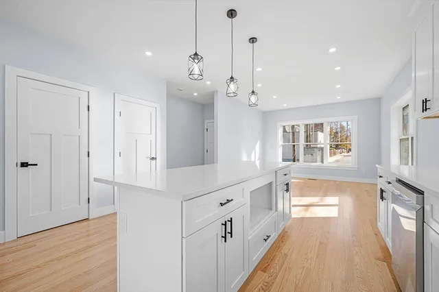 a large white kitchen with stainless steel appliances a lot of white cabinets and wooden floor