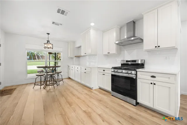 a kitchen with stainless steel appliances a white stove top oven a sink dishwasher and white cabinets with wooden floor