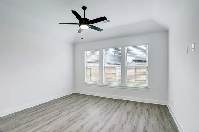 an empty room with wooden floor fan and windows