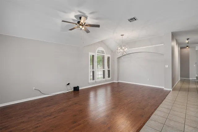 a view of an empty room with wooden floor and a ceiling fan