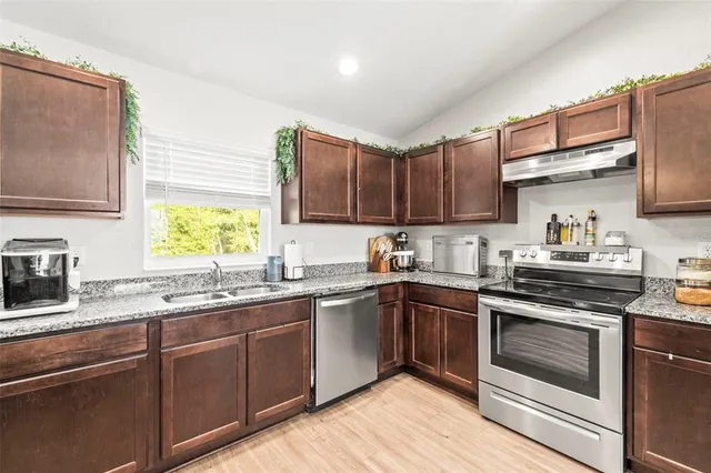 a kitchen with stainless steel appliances granite countertop a sink dishwasher stove and wooden floor