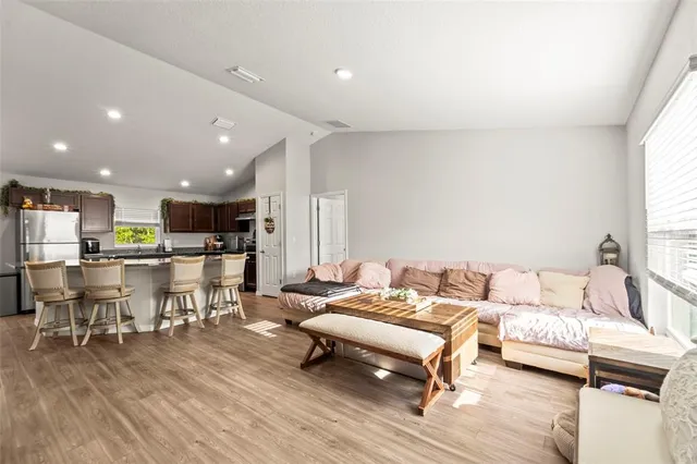 a living room with stainless steel appliances furniture wooden floor and a kitchen view