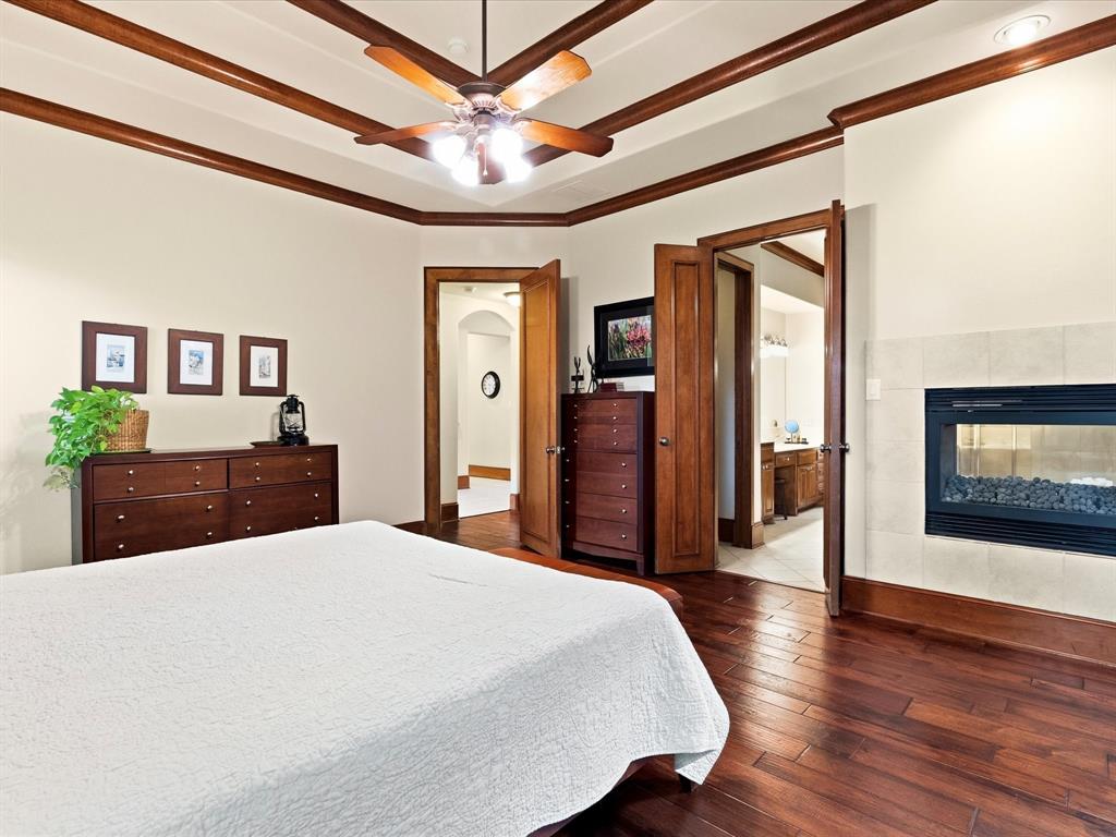 1615 Roma Lane Allen, TX 75013 - Photo 14 of 36 Bedroom featuring a built-in, double-sided fireplace, a tray ceiling with wood beam accents, a ceiling fan, and