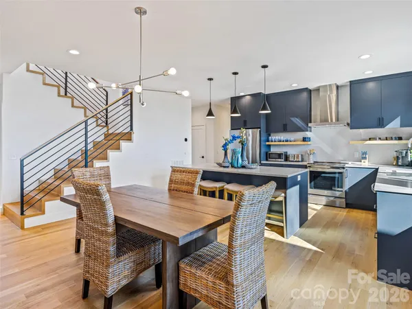 a kitchen with stainless steel appliances granite countertop a stove a refrigerator a kitchen island a dining table and chairs with wooden floor