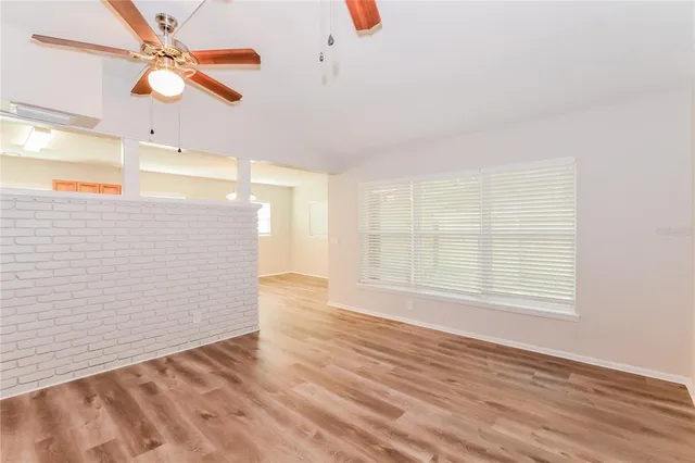 an empty room with wooden floor fan and windows