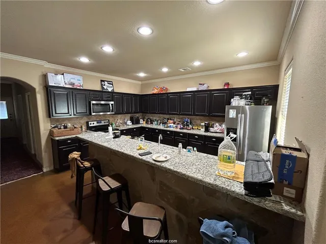 a kitchen with stainless steel appliances kitchen island granite countertop a sink refrigerator and cabinets