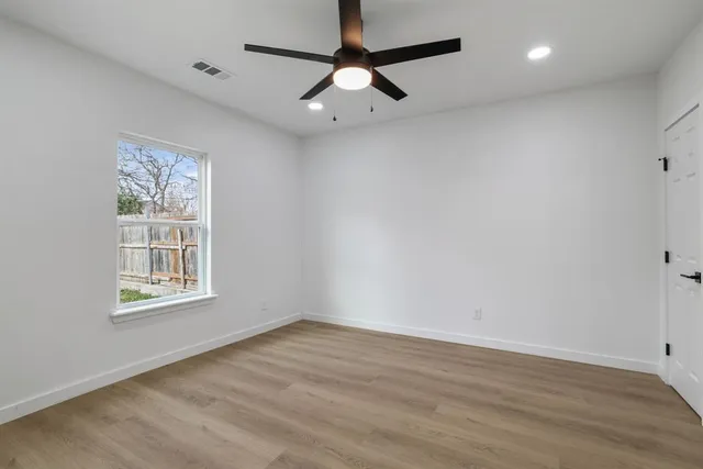 an empty room with wooden floor ceiling fan and windows