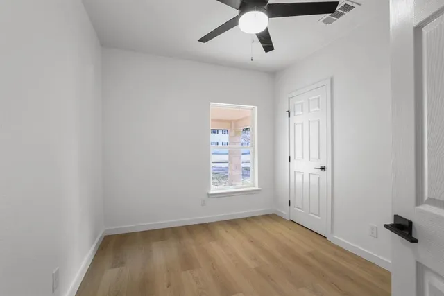 an empty room with wooden floor ceiling fan and windows