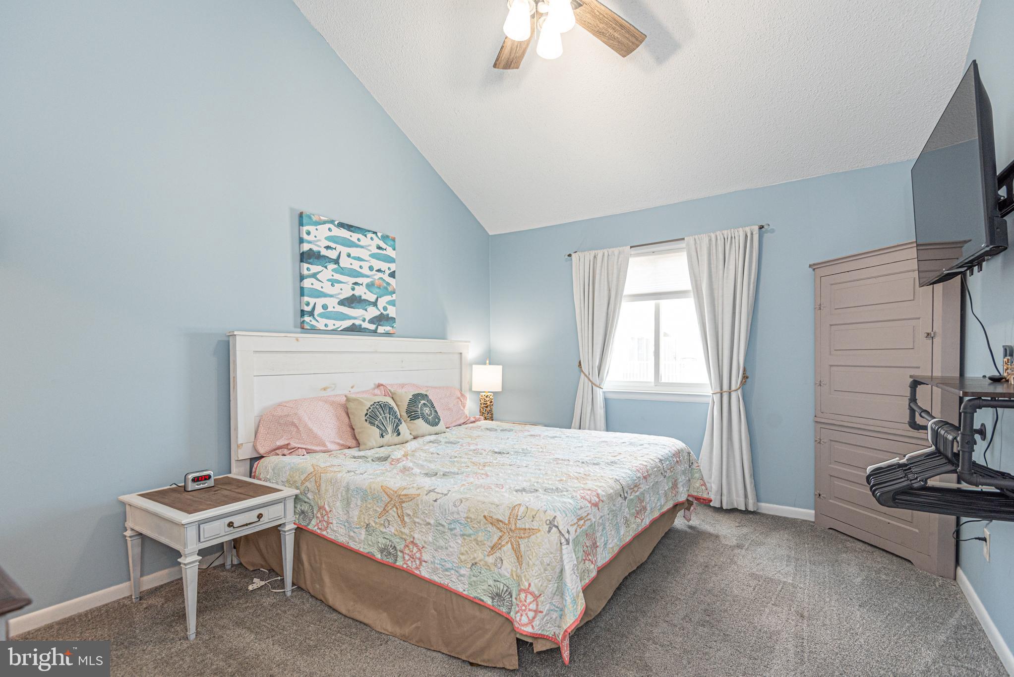 9203 Rusty Anchor Road, Unit A5 Ocean City, MD 21842 - Photo 18 of 60 a bedroom with a bed a couch and a flat tv screen on the dresser