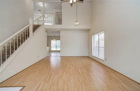 an empty room with wooden floor chandelier fan and windows