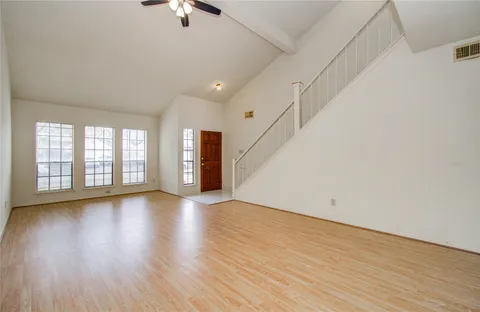 an empty room with wooden floor fan and windows
