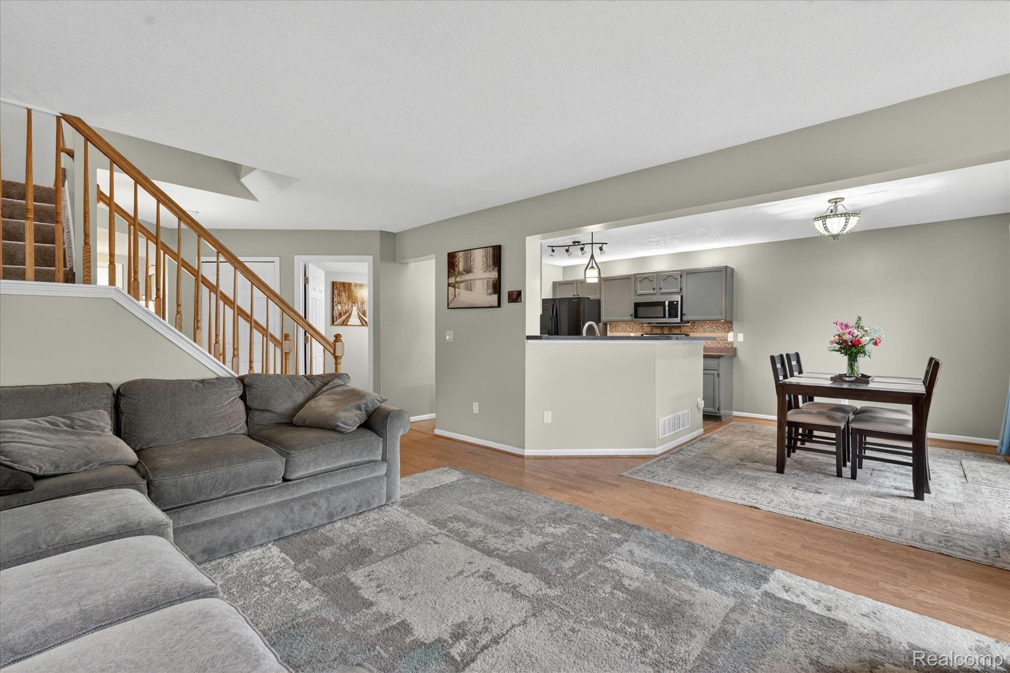 456 Lilly View Court Howell, MI 48843 - Photo 5 of 45 Open-concept living space featuring wood-finish flooring, a carpeted staircase with wood railings, and a dining area with a flush-mount ceiling light