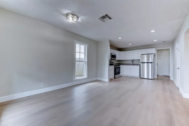 a view of empty room with wooden floor and kitchen