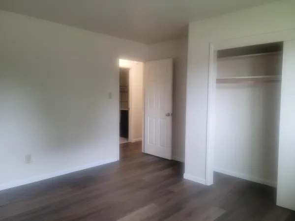 a view of an empty room with wooden floor & closet