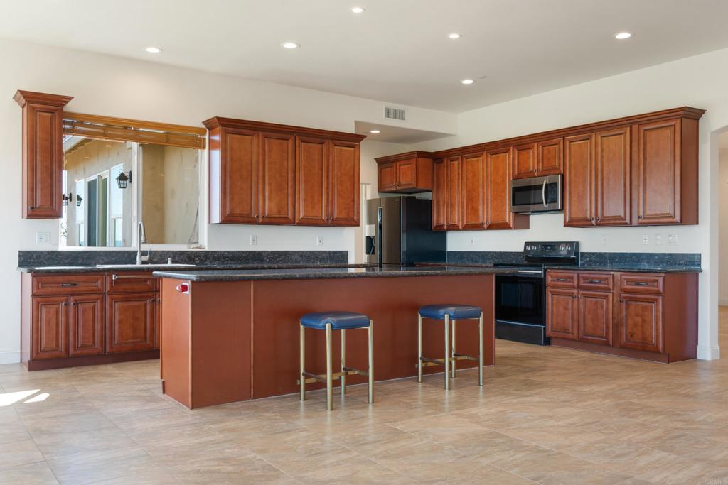 4261 Entrada Al Sol Bonsall, CA 92003 - Photo 12 of 49 a kitchen with stainless steel appliances granite countertop wooden cabinets a refrigerator and a stove top oven