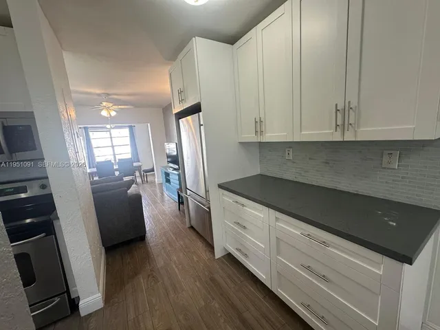 a kitchen with granite countertop a refrigerator a sink a stove and white cabinets