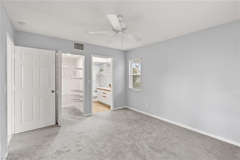 161 Wading Bird Circle, Unit L101 Naples, FL 34110 - Photo 18 of 44 Unfurnished bedroom with light colored carpet, connected bathroom, ceiling fan, and a textured ceiling