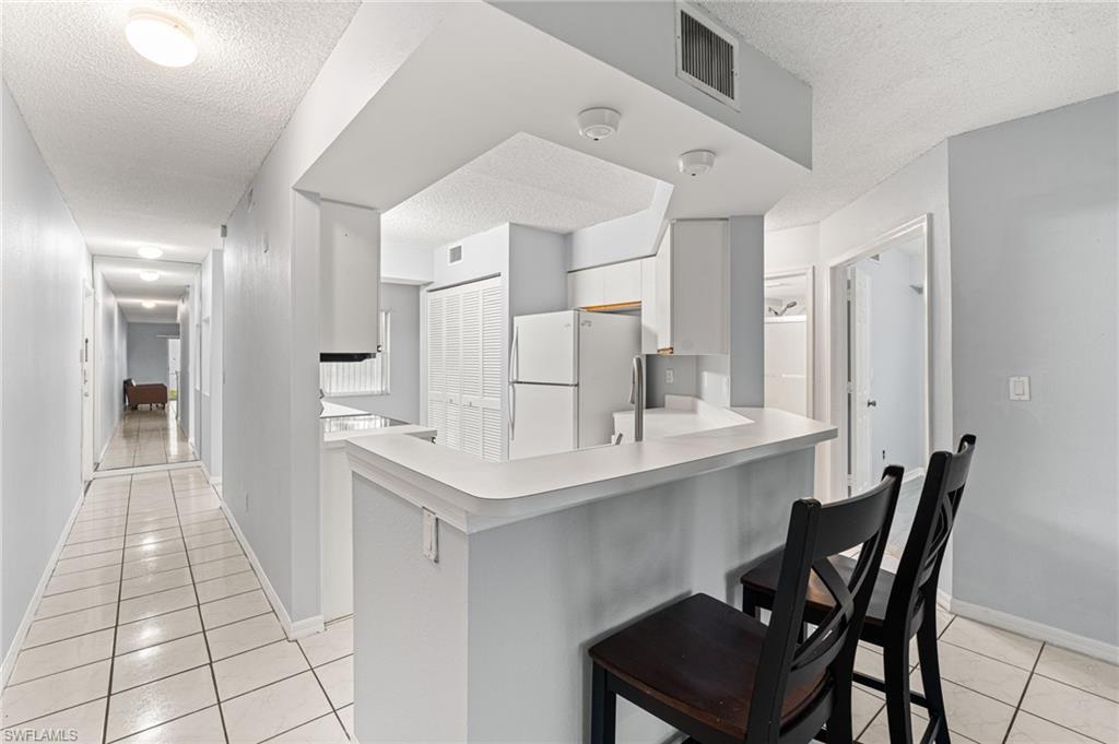 161 Wading Bird Circle, Unit L101 Naples, FL 34110 - Photo 9 of 44 Kitchen with light tile patterned flooring, a textured ceiling, a kitchen breakfast bar, light countertops, and freestanding refrigerator