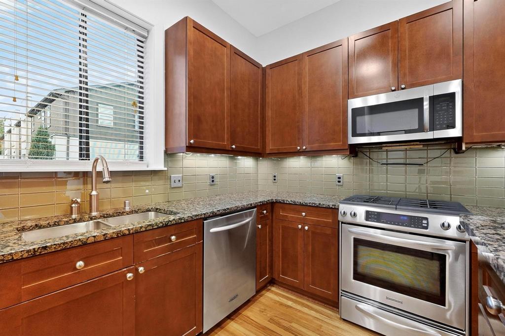 4211 Rawlins Street, Unit 528 Dallas, TX 75219 - Photo 5 of 14 Kitchen featuring a double basin stainless steel sink, granite countertops, wood-finish cabinetry, stainless steel appliances, and a tiled backsplash