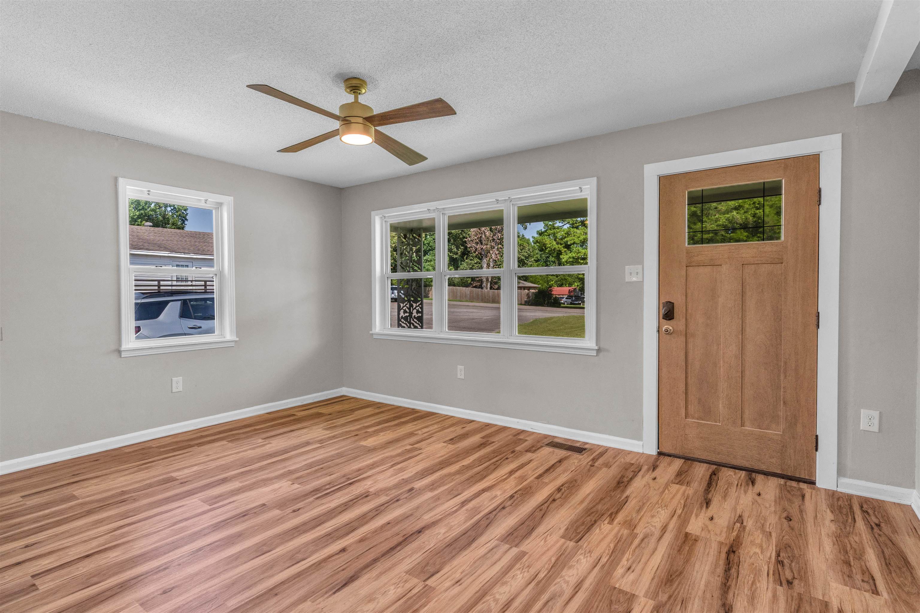 185 Henry Road Somerville, TN 38068 - Photo 4 of 21 Wood-finish flooring, light gray wall paint, multiple windows, ceiling fan with integrated lighting, and a wood entry door with a glass insert