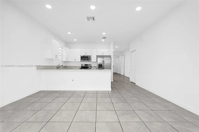 a view of an empty room with kitchen and a window