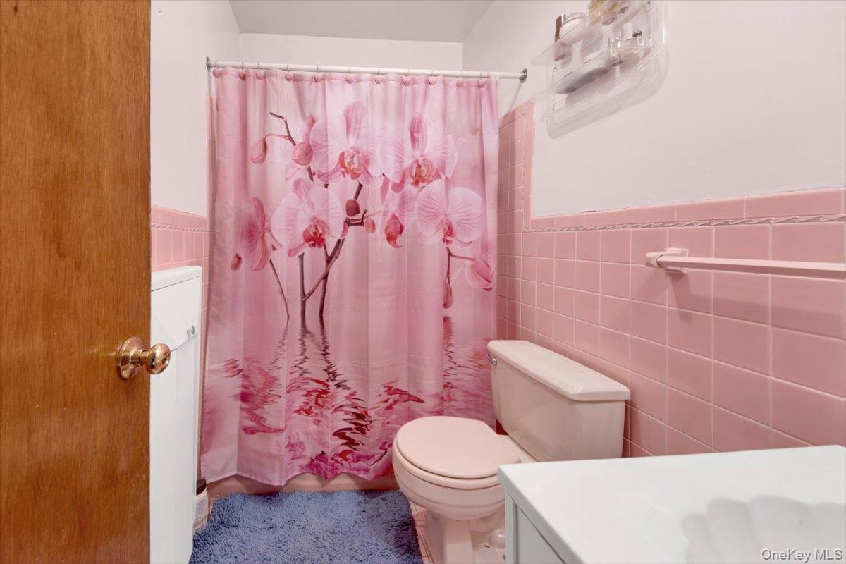 733 Rhinelander Avenue Bronx, NY 10462 - Photo 19 of 31 Full bathroom featuring vanity, curtained shower, tile walls, and a wainscoted wall