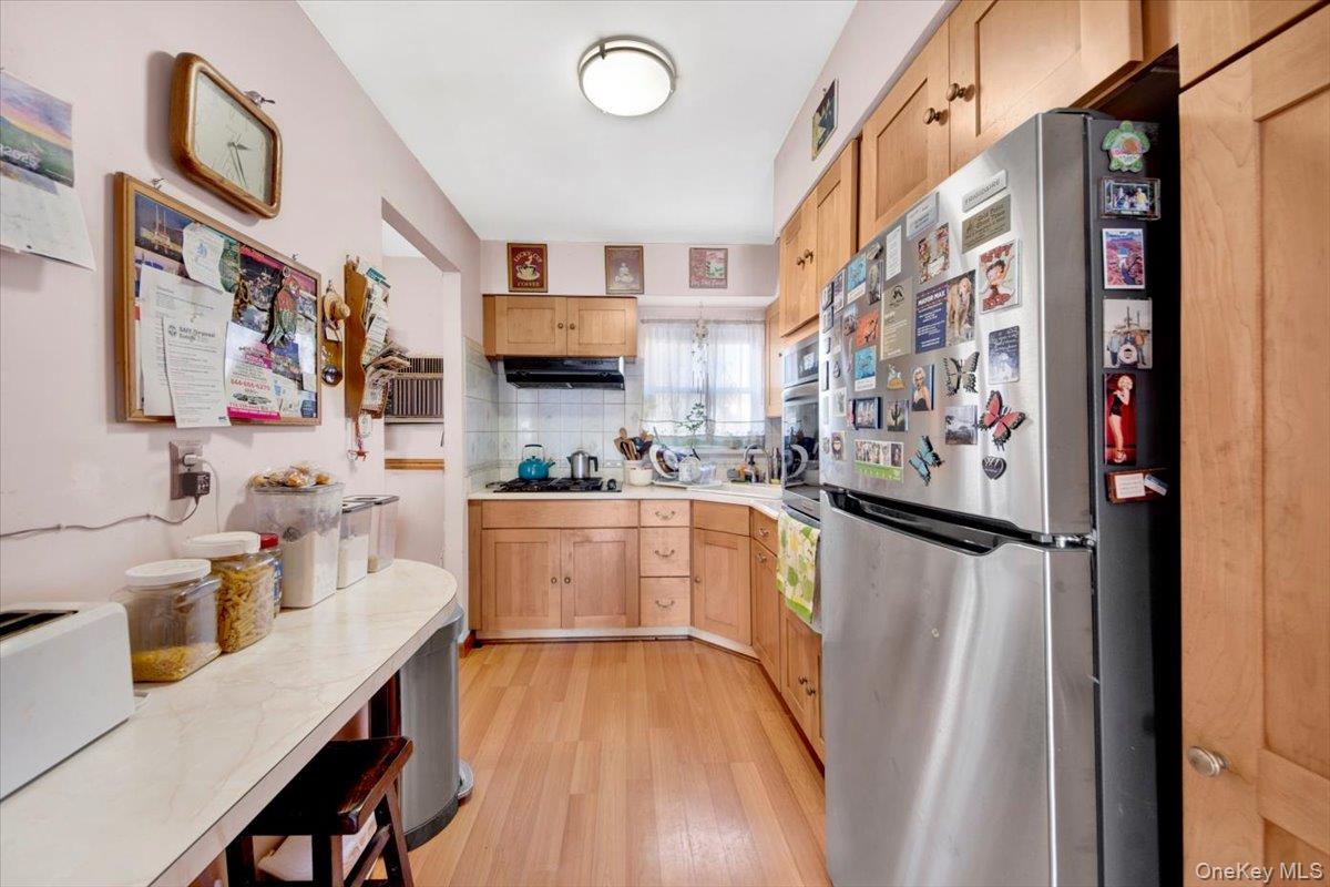 733 Rhinelander Avenue Bronx, NY 10462 - Photo 4 of 31 Kitchen featuring stainless steel appliances, light countertops, light brown cabinetry, light wood finished floors, and decorative backsplash