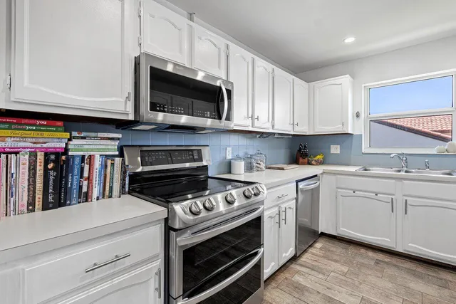 a kitchen with stainless steel appliances granite countertop grey cabinets a stove a sink and a microwave