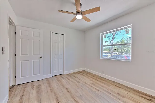 an empty room with wooden floor chandelier fan and windows