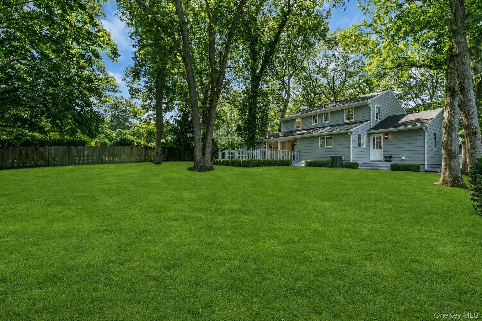 275 Pinewood Road Cutchogue, NY 11935 - Photo 34 of 45 Expansive green lawn, mature trees, privacy fencing, multi-level siding exterior, and a rear patio