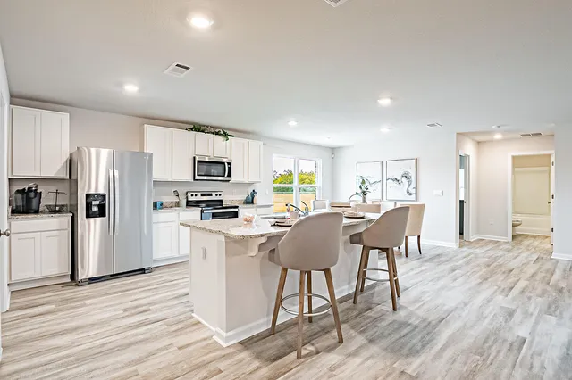 a kitchen with stainless steel appliances granite countertop a refrigerator a stove top oven a sink dishwasher a dining table and chairs with wooden floor